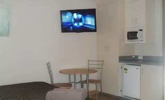 a small living room with a tv mounted on the wall , a dining table , and a kitchen area at Bali Hi Motel