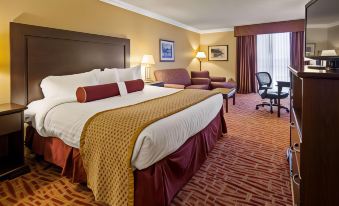 a large bed with a maroon blanket and gold throw is in the middle of a room with a chair , lamp , and couch at Best Western Plus Wilkes Barre Center City