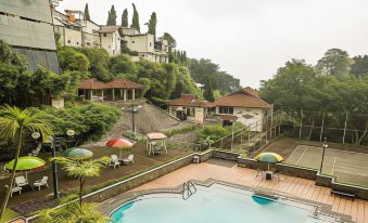a large swimming pool is surrounded by a pool area with umbrellas and lounge chairs , overlooking a hillside at Royal Tretes View Hotel & Convention