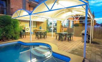 an outdoor dining area with a pool , umbrellas , and tables is shown next to a brick building at Ryde Inn