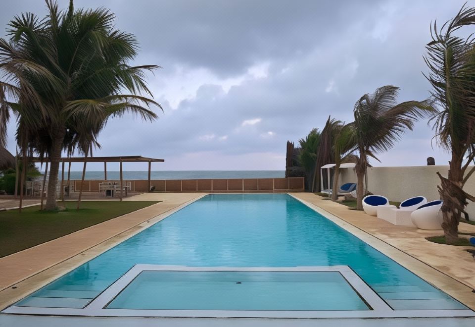 a large swimming pool with palm trees and lounge chairs is seen from the perspective of someone standing near the ocean at Dolphin Beach Resort