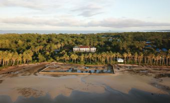 a large building with a pool in front of it surrounded by palm trees and water at Hotel Grand Papua Kaimana