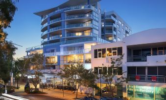 a modern , multi - level apartment building with balconies and trees in the background , at dusk at Scarborough Beach Resort