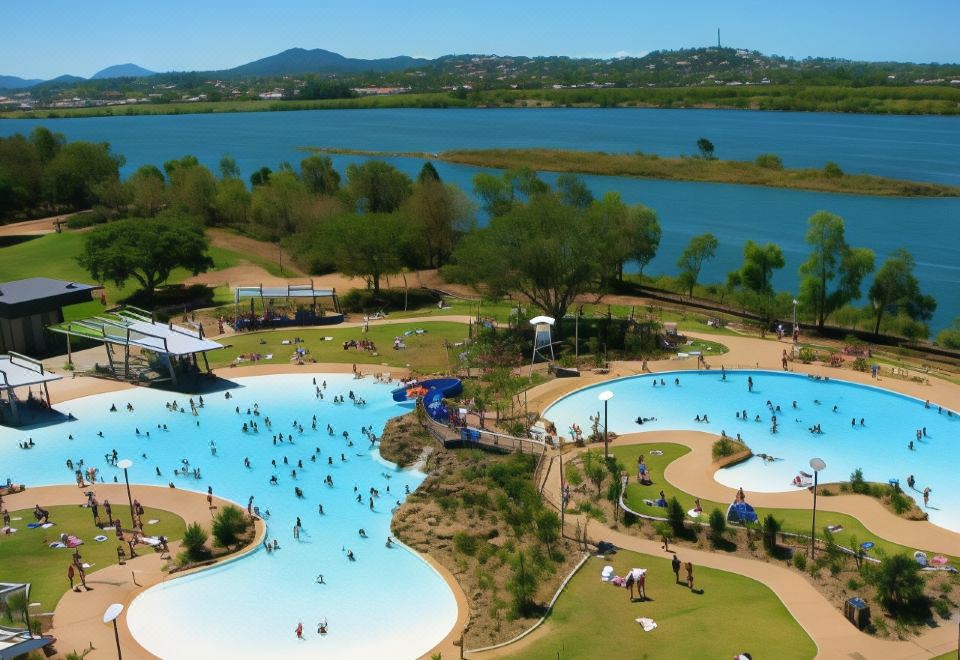 a large outdoor swimming pool surrounded by trees and grass , with people enjoying their time in the water at Rydges Mackay Suites, an EVT hotel