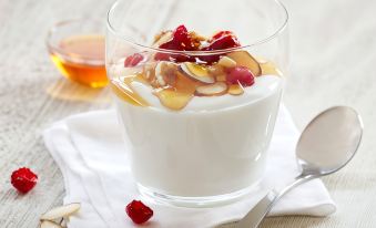 a glass of white yogurt with almonds and cherries is placed on a napkin , accompanied by a spoon and a glass of red liquid at Residence Inn Stockton