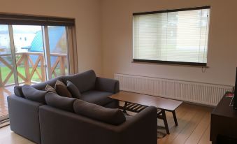 a living room with a gray couch , wooden floor , and a window with blinds , as well as a small coffee table at Ume