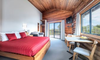 a cozy bedroom with a wooden bed , red bedding , and a dining table in the corner at Shining Star Beachfront Accommodation