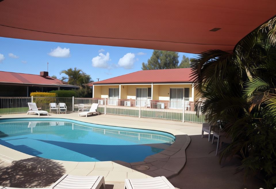 a large swimming pool is surrounded by white lounge chairs and a red - roofed building with multiple balconies at Emerald Explorers Inn