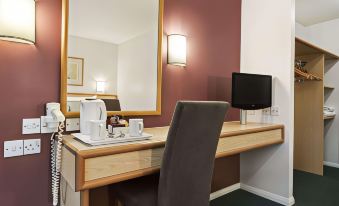 a hotel room with a desk , chair , and television in front of a large mirror at Days Inn by Wyndham Sedgemoor M5