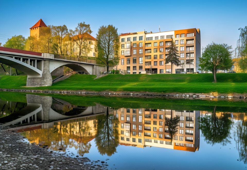 a large building with a reflection in the water , surrounded by grass and trees , near a bridge at Hampton by Hilton Oswiecim