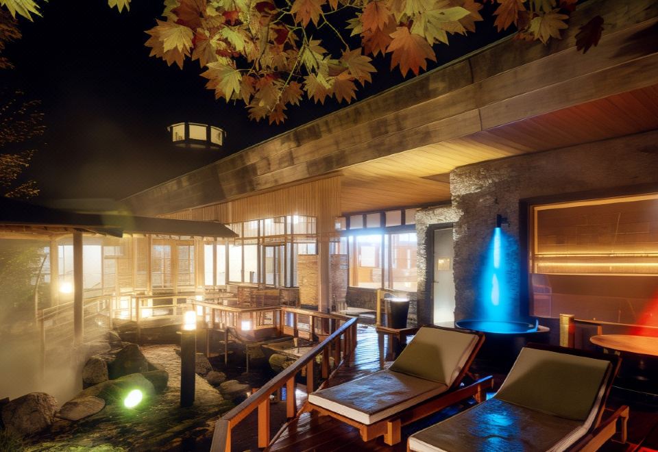 a luxurious indoor spa with large windows , wooden benches , and a waterfall , illuminated by lights at night at Noboribetsu Grand Hotel
