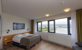 a bedroom with a large window overlooking the ocean , featuring a bed and a flat - screen tv at Hotel Selfoss