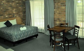 a modern bedroom with brick walls , wooden furniture , and a large window , decorated with a bedspread , curtains , and a dining table at Motel Goolwa