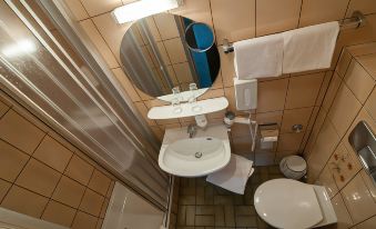 a small bathroom with a sink , toilet , and shower area , along with various personal care items at Akzent Hotel Schranne