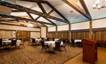 a large , well - lit room with wooden beams and a carpet floor has several tables and chairs set up for an event at Best Western University Inn