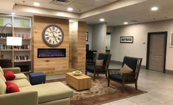 a modern living room with a wooden wall , large clock on the wall , and comfortable seating arrangements at Country Inn & Suites by Radisson, Emporia, VA