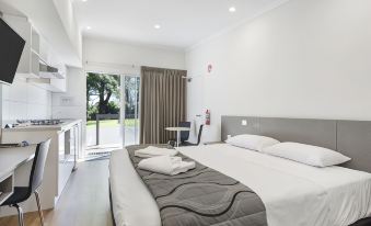 a modern hotel room with a large bed , white walls , and a balcony overlooking the city at Discovery Parks - Perth Airport