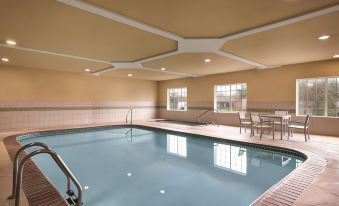 a large indoor swimming pool with a wooden deck and two chairs , under a white ceiling at Country Inn & Suites by Radisson, Rocky Mount, NC