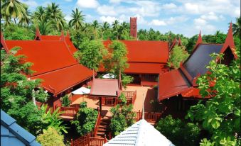 a traditional thai building with red roofs and wooden balconies , surrounded by lush greenery and clear blue skies at Baan Amphawa Resort & Spa