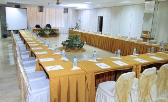a conference room set up for a meeting , with multiple tables and chairs arranged in a semicircle at Hotel Cianjur Cipanas