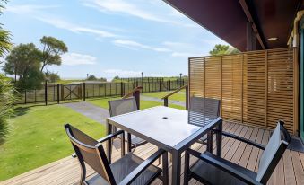 a wooden deck with a table and chairs , overlooking a golf course and the ocean at Shining Star Beachfront Accommodation