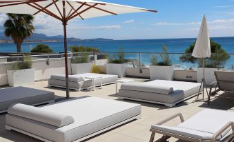 a rooftop patio with white lounge chairs , an umbrella , and a view of the ocean at Mercure Villeneuve Loubet Plage
