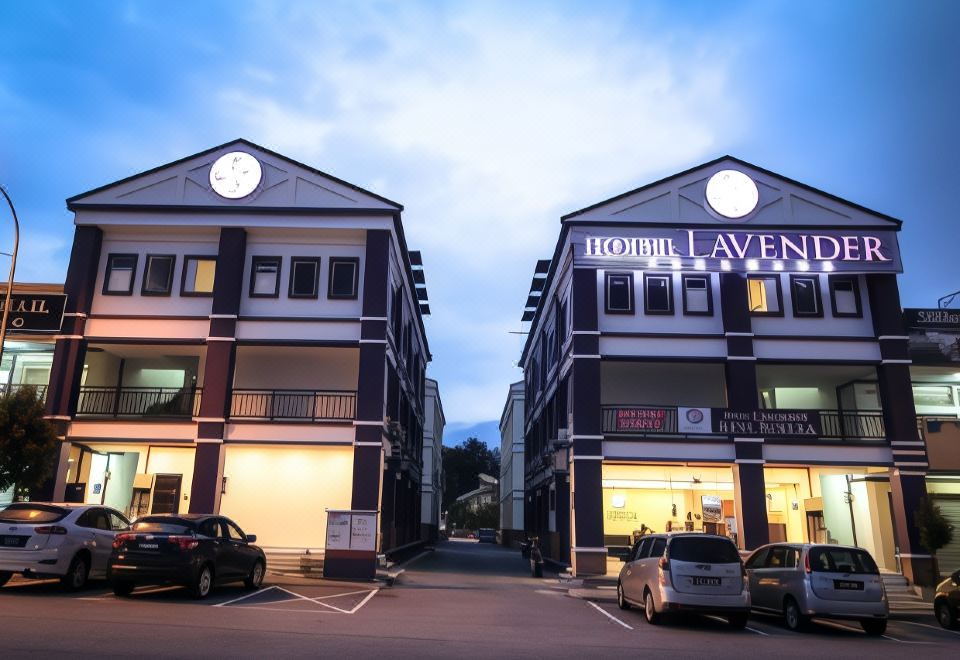 "a parking lot with multiple cars and buildings , including one that says "" hotel lavene ,"" under a blue sky" at Hotel Lavender Senawang