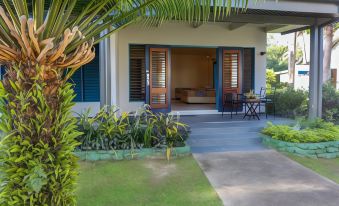 a house with blue doors and windows , surrounded by green grass and palm trees , under the shade of trees at Fiji Hideaway Resort and Spa