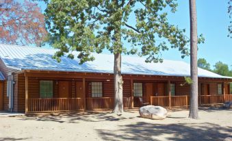 a wooden cabin with a large tree in front of it , surrounded by rocks and grass at New Hochatown Lodge