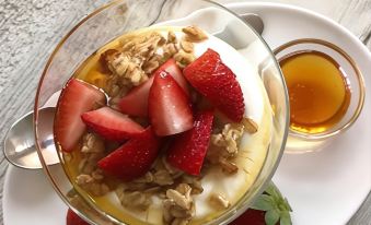 a white plate with a glass bowl filled with yogurt , topped with strawberries and granola , sits on a wooden table at Residence Inn Fort Lauderdale Weston