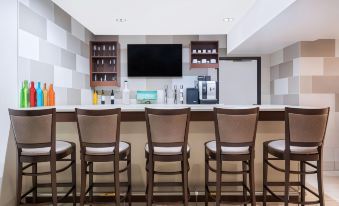 a hotel bar with a long counter , several chairs , and a flat - screen tv mounted on the wall at Ramada by Wyndham Minneapolis Golden Valley