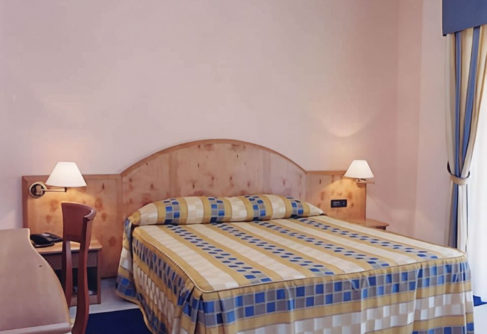 a large bed with a blue and white striped comforter is in a room with two lamps on either side of the headboard at Hotel Daniela