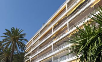 a tall white building with yellow accents is surrounded by palm trees and another smaller tree at Hotel Victoria