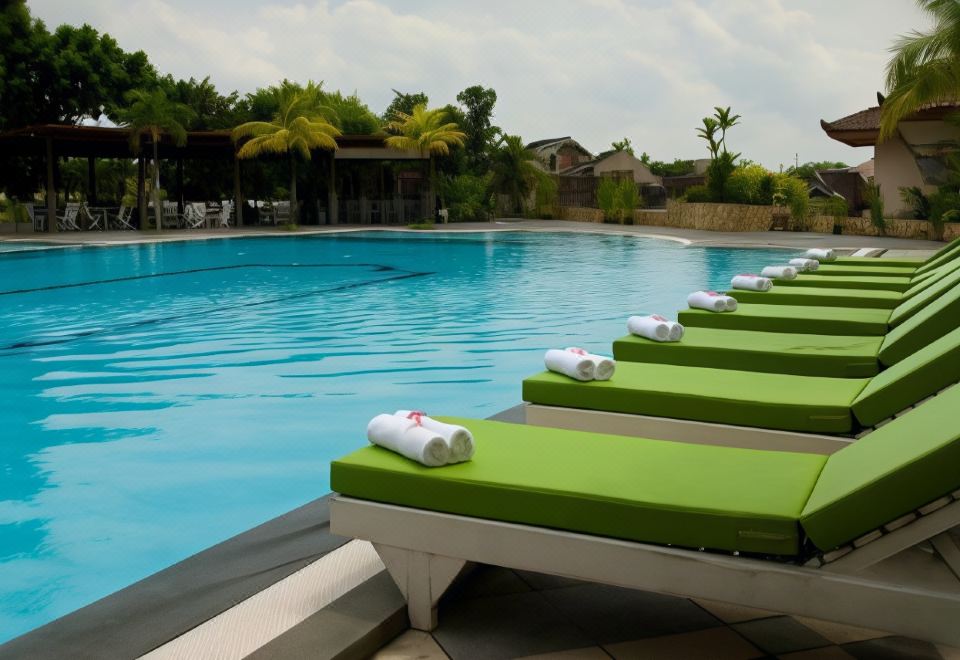 a large outdoor swimming pool surrounded by lounge chairs and umbrellas , providing a relaxing atmosphere at The Sunan Hotel Solo