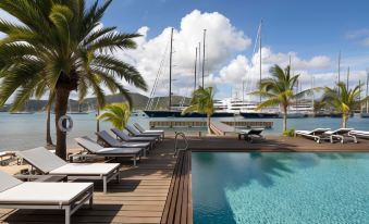 a large outdoor pool surrounded by lounge chairs and umbrellas , with several sailboats docked in the water at South Point Antigua