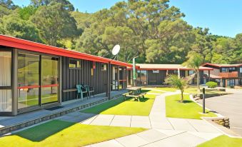 a modern building with red roof and large windows , surrounded by green grass and trees , under a clear blue sky at Anglers Lodge