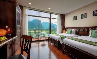 a modern hotel room with large windows offering a view of the mountains , featuring two beds and wooden flooring at Tam Coc La Montagne Resort & Spa