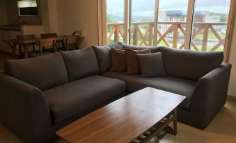 a large gray couch is sitting in a living room with a wooden coffee table and a view of the ocean at Ume