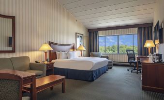 a large bed with a white and blue comforter is in the middle of a room with two chairs , lamps , and a window at DoubleTree by Hilton Pittsburgh Monroeville Convention Center