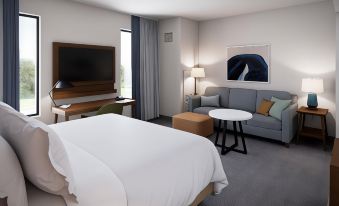 a modern hotel room with a white bed , couch , coffee table , and tv . also a dining table in the room at Staybridge Suites Pittsburgh Airport