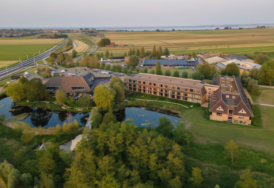 aerial view of a large building surrounded by a grassy field and a body of water at Van der Valk Hotel Volendam