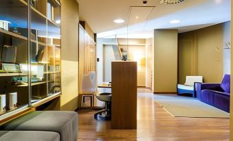 a modern office space with wooden floors , white walls , and large windows , featuring a desk , chair , bookshelves , and comfortable seating at Axis Porto Business & Spa Hotel