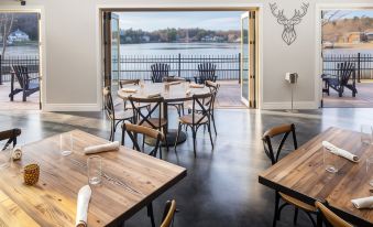 a modern restaurant with wooden tables and chairs , a view of the water through large windows at Saranac Waterfront Lodge, Trademark Collection by Wyndham