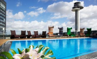 a rooftop pool surrounded by lounge chairs and umbrellas , with a tower in the background at Clarion Hotel Arlanda Airport Terminal