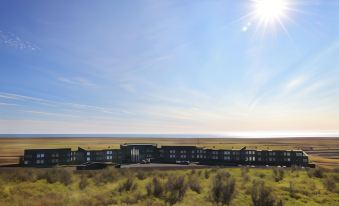 a large building is situated in a field with the sun shining brightly behind it at Fosshotel Glacier Lagoon