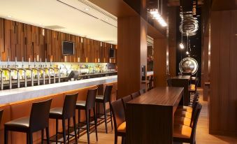 a modern bar with wooden furniture , a long counter , and multiple chairs , under hanging lights at Clayton Hotel Chiswick