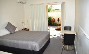 a bedroom with a bed , table , and chairs is shown with an open door leading to a patio at Redland Bay Motel
