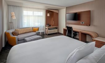 a modern hotel room with a large bed , desk , and couch , along with a tv and other amenities at Courtyard Schenectady at Mohawk Harbor