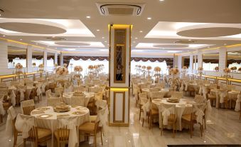 a large , well - lit banquet hall with multiple tables set for a formal event , each table having its own unique arrangement of flowers and at Emirtimes Hotel&Spa - Tuzla
