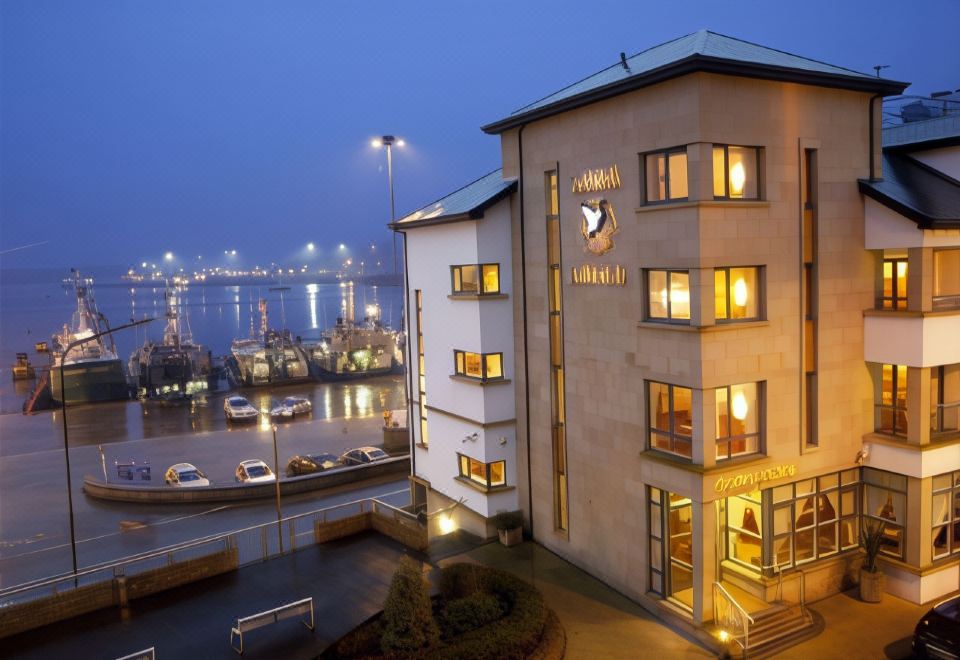 a building with a clock on the side is lit up at night , overlooking a harbor filled with boats at Tara Hotel